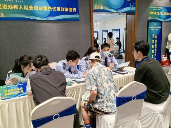 (图说:在税惠助残政策宣传专区,税务干部为纳税人缴费人解答税费政策问题,辅导个税app汇算操作)